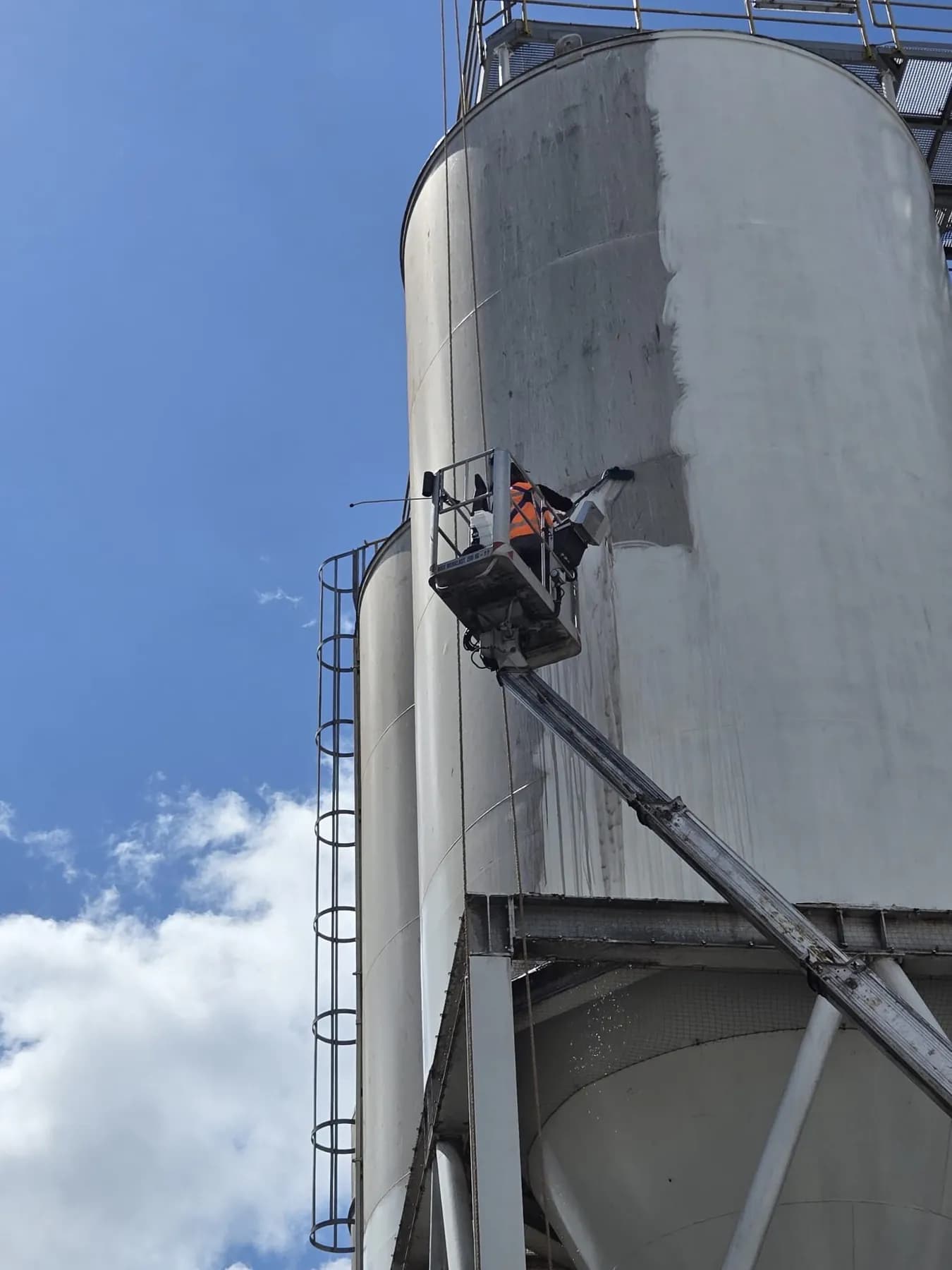 Medewerker reinigt een silo vanaf een hoogwerker; het verschil tussen schoon en vuil is goed zichtbaar