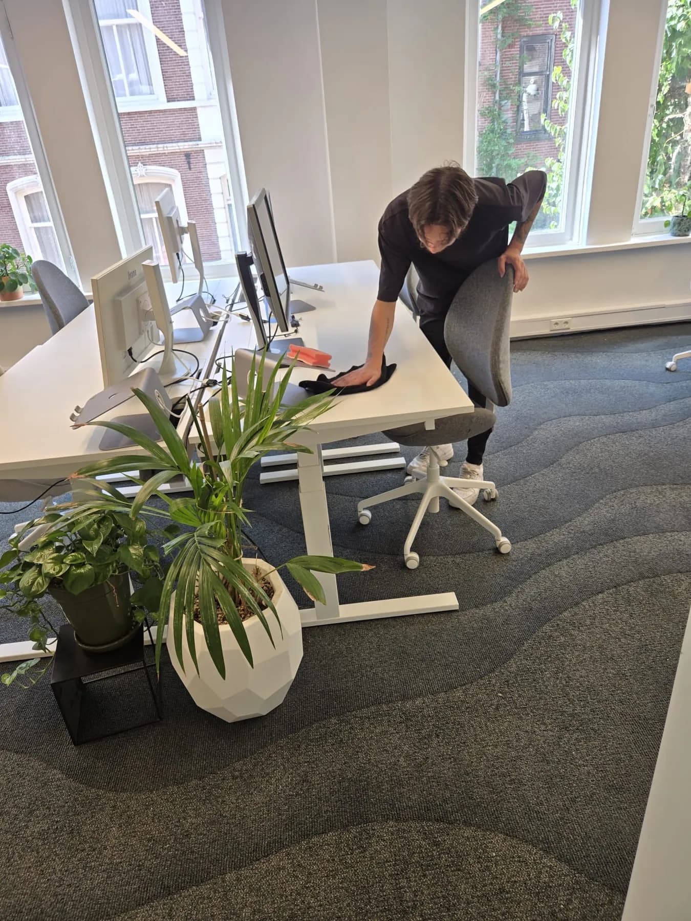 Medewerker neemt een bureau af met een microvezeldoek in een licht kantoor