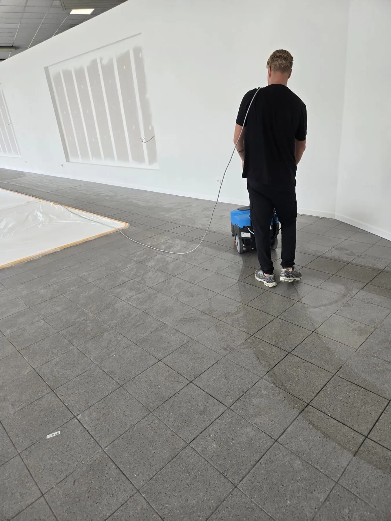 Medewerker reinigt een grijze tegelvloer met een compacte schrobzuigmachine in een lege showroom