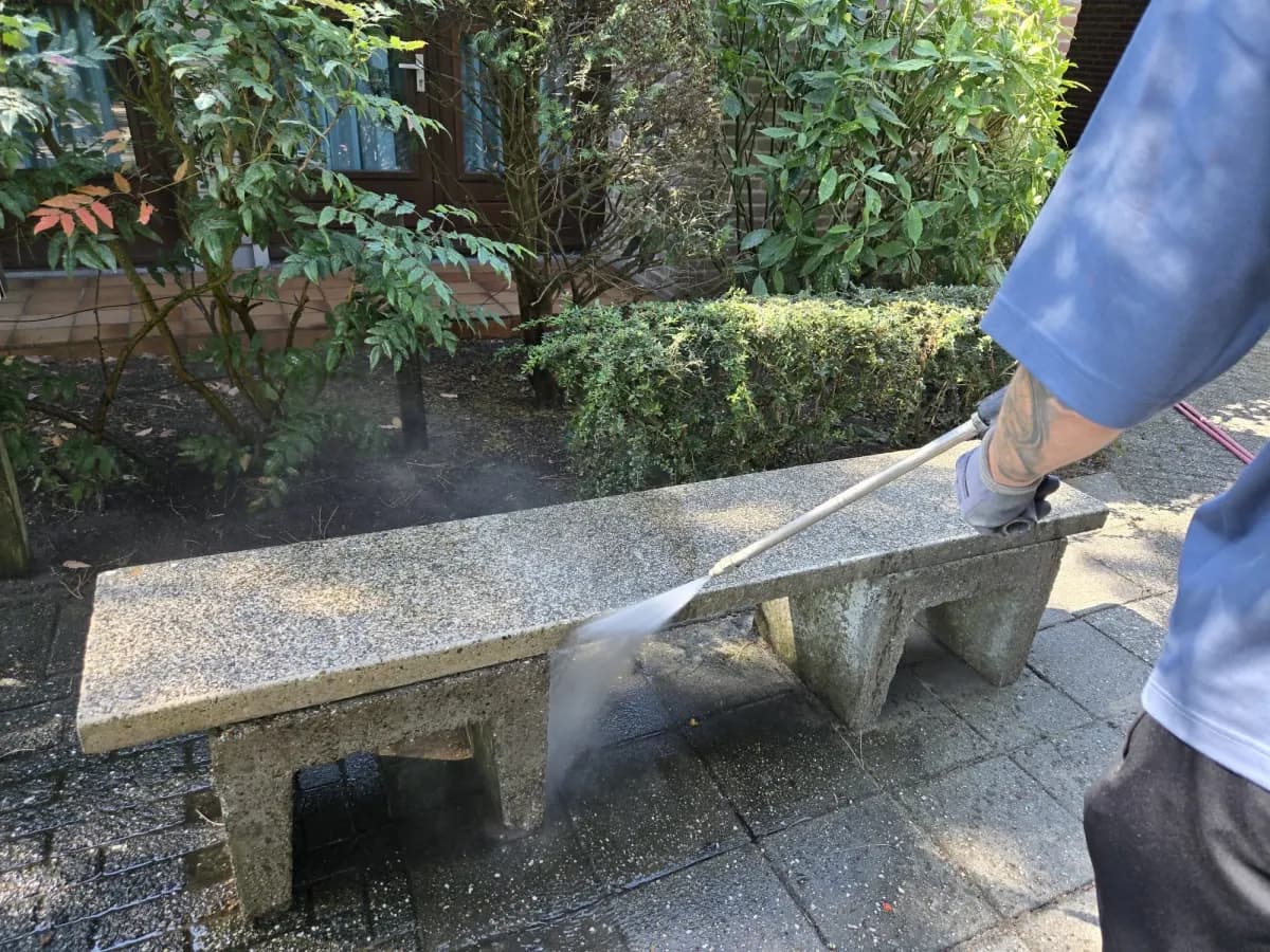 Medewerker reinigt een stenen buitenoppervlak met hoge druk