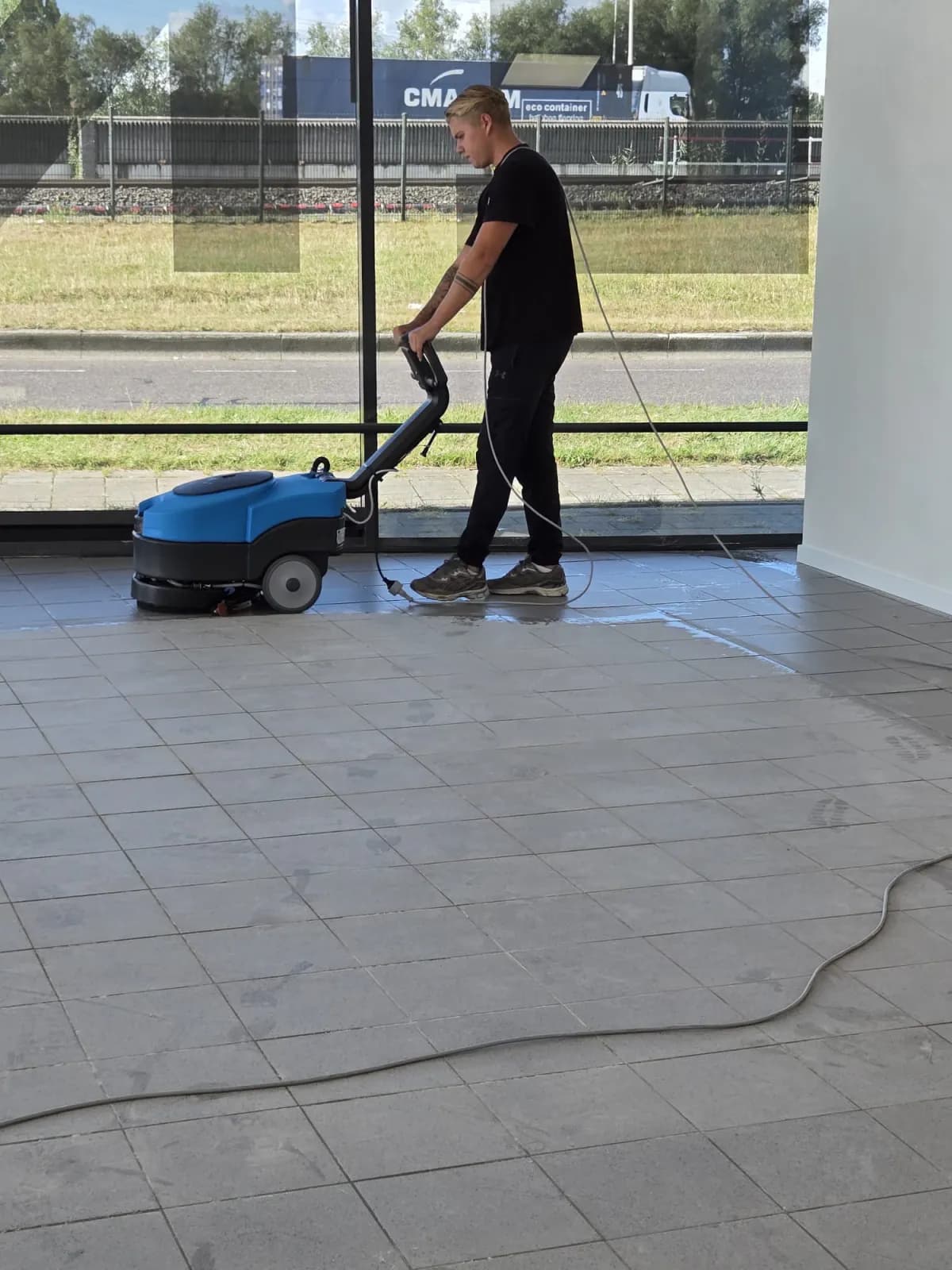 Medewerker reinigt een tegelvloer met een schrobzuigmachine